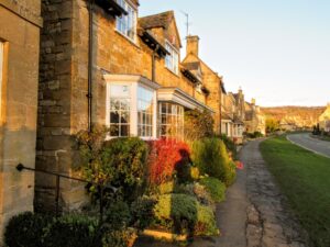 Visiting the Cotswolds in November. Yellow Cotswolds stone with colourful autumnal bushes around.