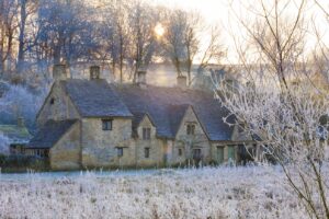 The sun setting on hoar frost on Arlington Row and Rack Isle in the Cotswold village of Bibury, Gloucestershire UK on a Go Cotswolds tour